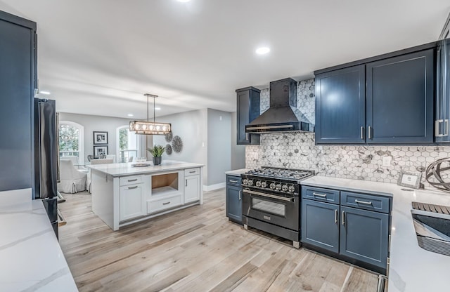 kitchen featuring wall chimney range hood, hanging light fixtures, backsplash, high end black range, and light hardwood / wood-style floors