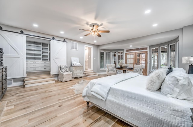 bedroom with french doors, ceiling fan, a barn door, and light hardwood / wood-style floors