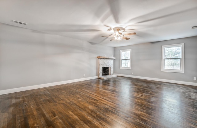 unfurnished living room with a brick fireplace, dark wood-type flooring, and ceiling fan