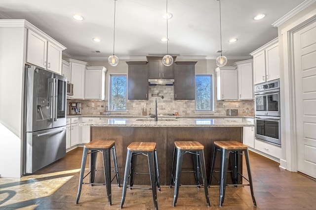 kitchen featuring stainless steel appliances, hanging light fixtures, a kitchen island with sink, and a breakfast bar area