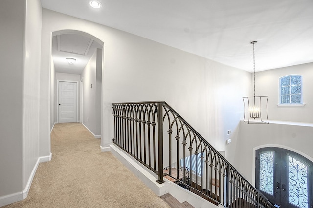 hall featuring light colored carpet, a notable chandelier, and french doors