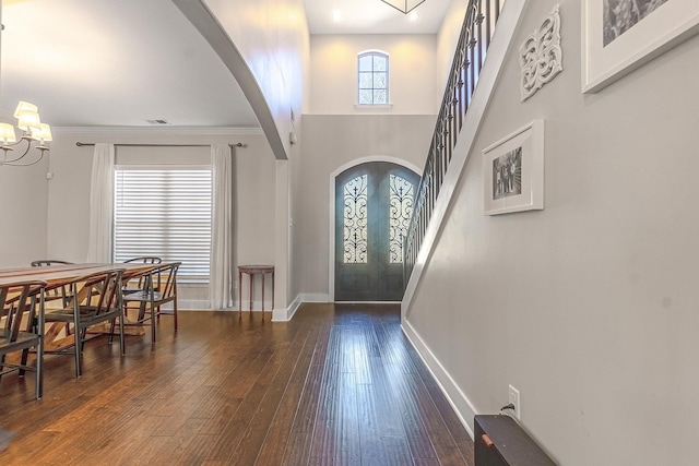 entrance foyer with dark wood-type flooring, an inviting chandelier, a high ceiling, ornamental molding, and french doors