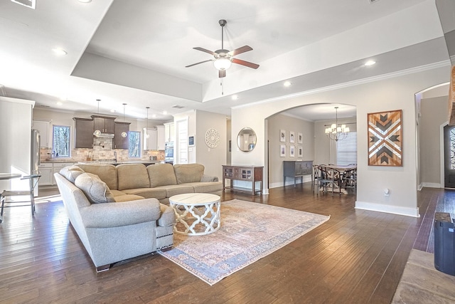 living room featuring a raised ceiling, ornamental molding, dark wood-type flooring, and ceiling fan with notable chandelier