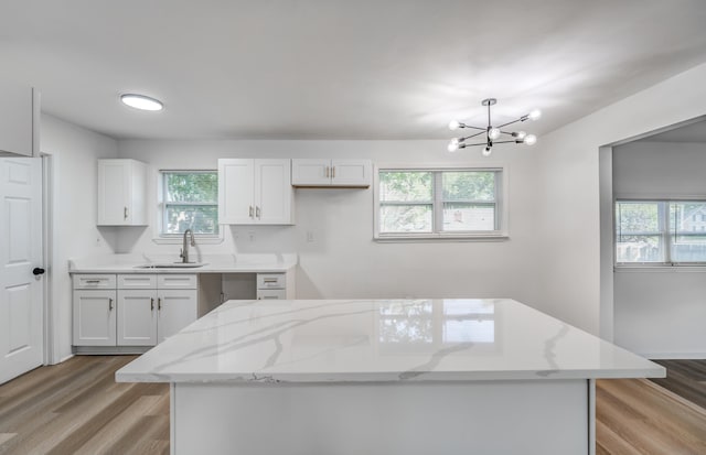 kitchen with white cabinetry, sink, light stone counters, and an inviting chandelier