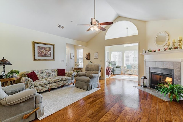 living room featuring a tiled fireplace, hardwood / wood-style flooring, high vaulted ceiling, and ceiling fan