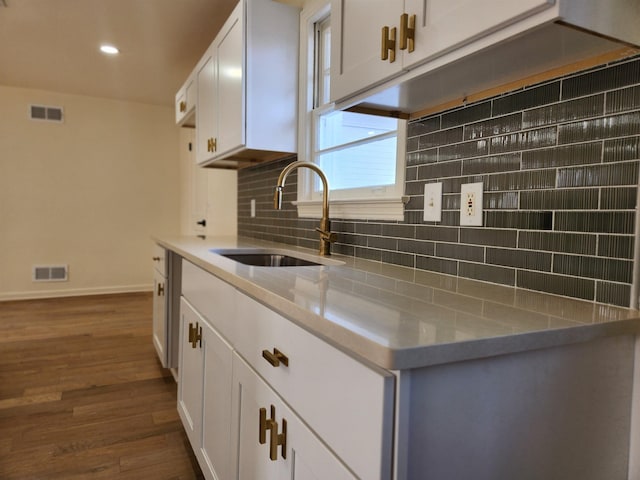 kitchen with tasteful backsplash, sink, white cabinets, light stone countertops, and dark wood-type flooring