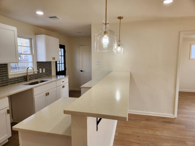 kitchen with tasteful backsplash, decorative light fixtures, sink, and white cabinets