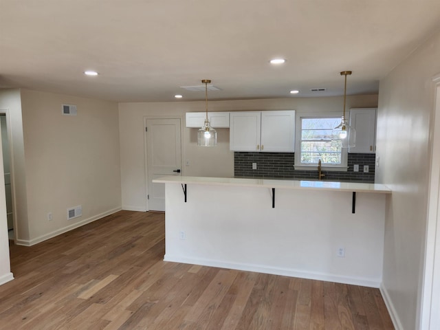 kitchen featuring white cabinetry, pendant lighting, a kitchen bar, and light wood-type flooring