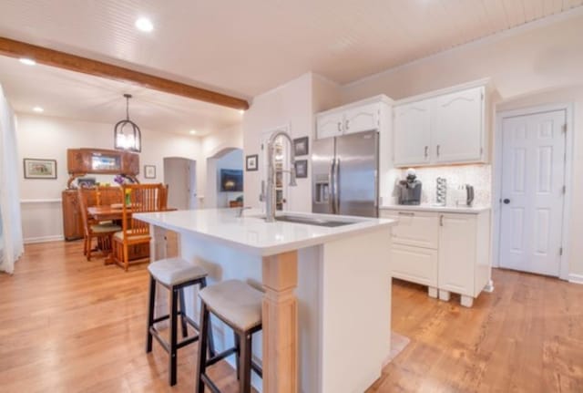 kitchen featuring stainless steel refrigerator with ice dispenser, a center island with sink, white cabinets, and beam ceiling