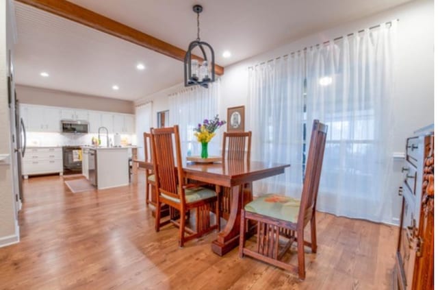 dining room with a notable chandelier, beam ceiling, and light wood-type flooring