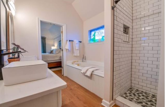 bathroom featuring vanity, hardwood / wood-style floors, vaulted ceiling, and shower with separate bathtub