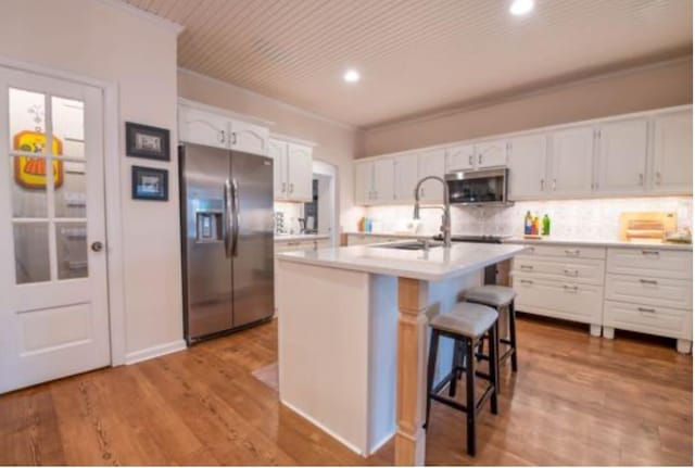 kitchen featuring appliances with stainless steel finishes, white cabinetry, sink, crown molding, and a center island with sink