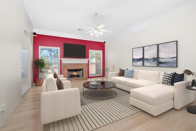 living area featuring visible vents, light wood-style flooring, ceiling fan, ornamental molding, and a brick fireplace