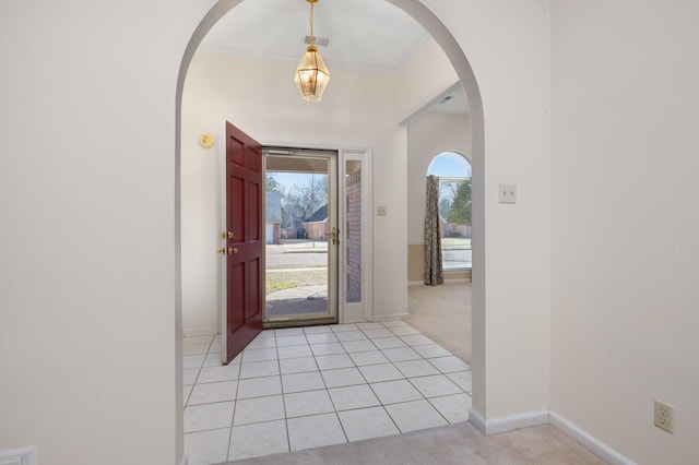 foyer with arched walkways, light tile patterned flooring, light colored carpet, visible vents, and baseboards