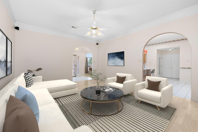 living room with arched walkways, light wood-style flooring, a ceiling fan, visible vents, and crown molding