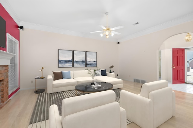 living area with arched walkways, visible vents, light wood-style floors, ornamental molding, and a ceiling fan