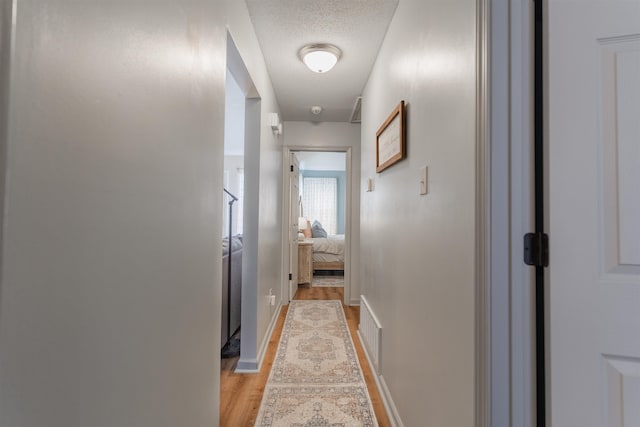 corridor with light hardwood / wood-style flooring and a textured ceiling