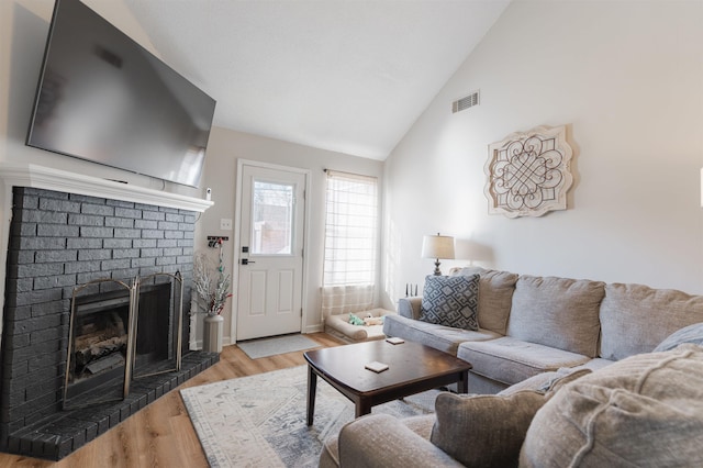 living room with light hardwood / wood-style floors, vaulted ceiling, and a brick fireplace