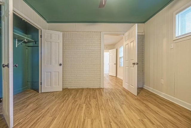 unfurnished bedroom with light hardwood / wood-style flooring, a closet, ceiling fan, and brick wall