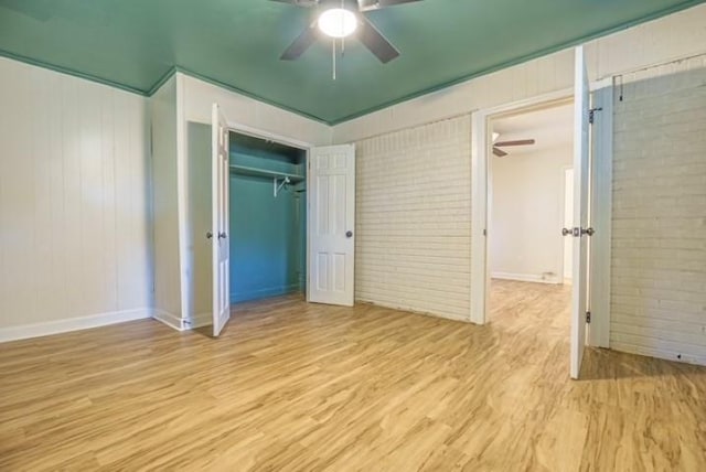 unfurnished bedroom with light hardwood / wood-style flooring, a closet, ceiling fan, and brick wall