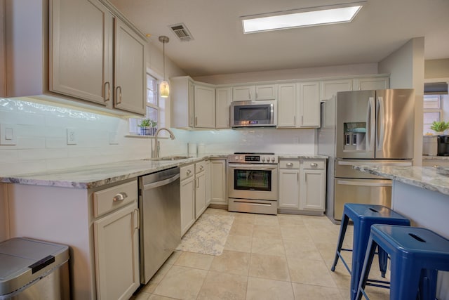 kitchen with appliances with stainless steel finishes, decorative light fixtures, sink, a kitchen bar, and light stone countertops