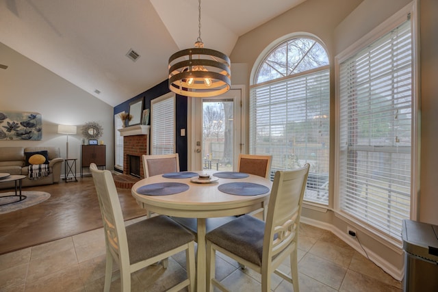 dining area featuring an inviting chandelier, light tile patterned flooring, high vaulted ceiling, and a brick fireplace