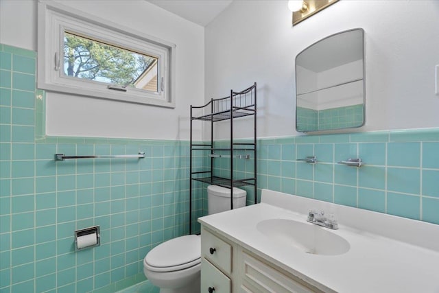 bathroom with tile walls, a wainscoted wall, vanity, and toilet