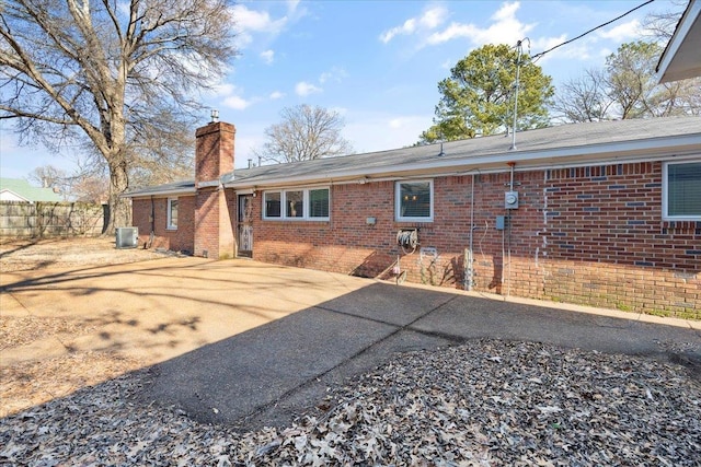 rear view of house with brick siding, a chimney, central AC unit, and fence