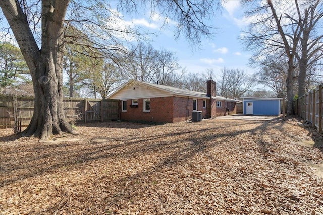 back of property featuring a fenced backyard, a chimney, an outbuilding, central AC, and brick siding