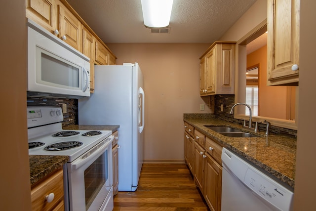 kitchen featuring sink, white appliances, hardwood / wood-style floors, tasteful backsplash, and dark stone counters