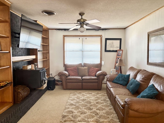 living room featuring ceiling fan, carpet floors, ornamental molding, a textured ceiling, and a wood stove