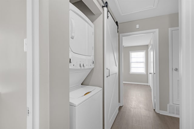 laundry room with stacked washer and clothes dryer, a barn door, and light hardwood / wood-style flooring