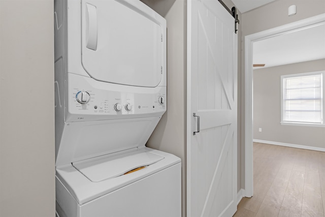 clothes washing area featuring a barn door, stacked washer and clothes dryer, and light wood-type flooring