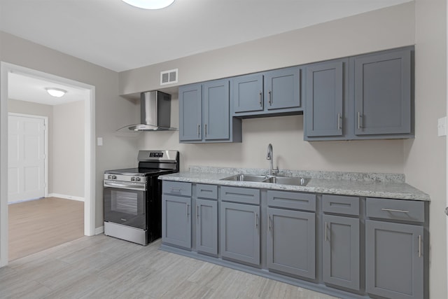 kitchen featuring wall chimney exhaust hood, sink, light stone counters, stainless steel electric range, and light wood-type flooring