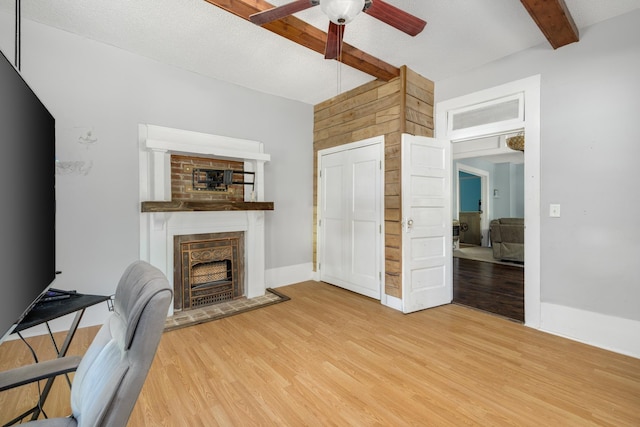 living room with ceiling fan, wood-type flooring, beam ceiling, and a textured ceiling