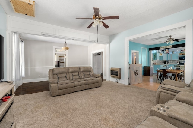 living room featuring ceiling fan, carpet flooring, heating unit, and a textured ceiling