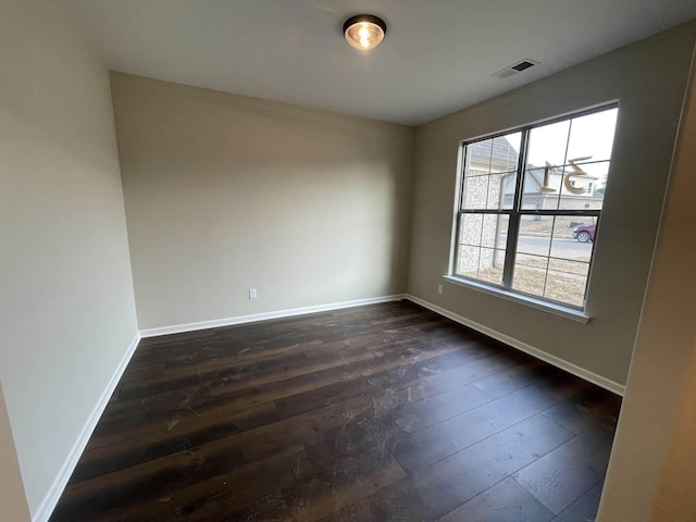 empty room with dark wood-style floors, visible vents, and baseboards