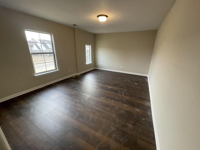 empty room with dark wood-type flooring, visible vents, and baseboards