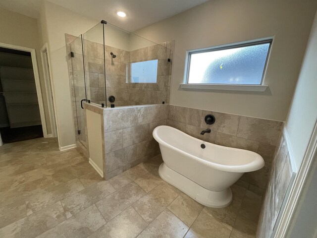 full bath featuring a stall shower, a freestanding bath, and tile walls