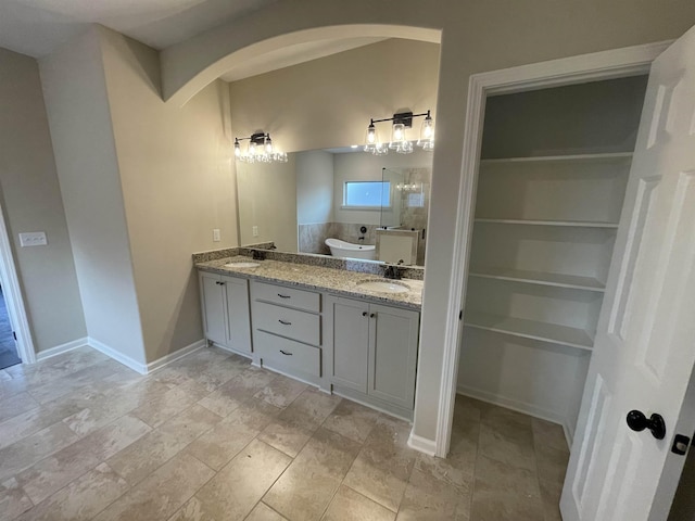 bathroom featuring double vanity, baseboards, a tile shower, and a sink