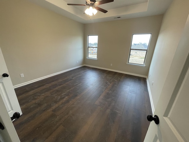 unfurnished room with baseboards, visible vents, a raised ceiling, and dark wood-type flooring