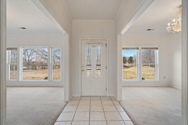 entryway with light carpet, a notable chandelier, ornamental molding, and a healthy amount of sunlight