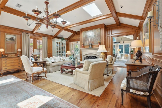 living room featuring a notable chandelier, wooden walls, vaulted ceiling with skylight, and light wood-type flooring