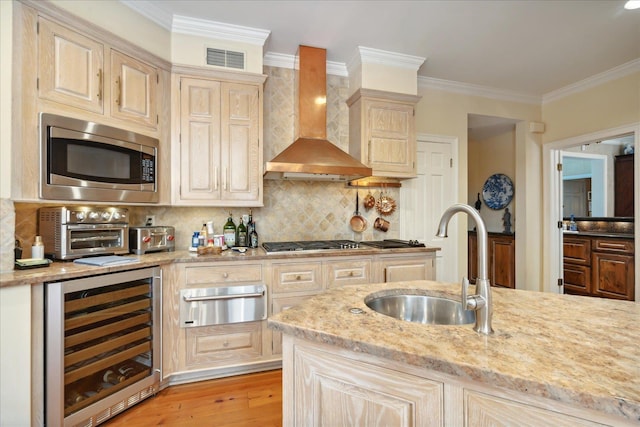 kitchen featuring sink, appliances with stainless steel finishes, beverage cooler, light stone countertops, and wall chimney range hood