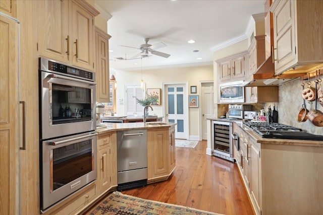 kitchen featuring appliances with stainless steel finishes, beverage cooler, light brown cabinets, crown molding, and wall chimney range hood