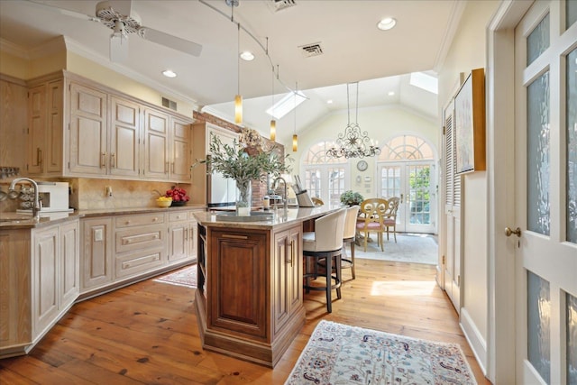 kitchen featuring decorative light fixtures, an island with sink, lofted ceiling, a kitchen bar, and crown molding