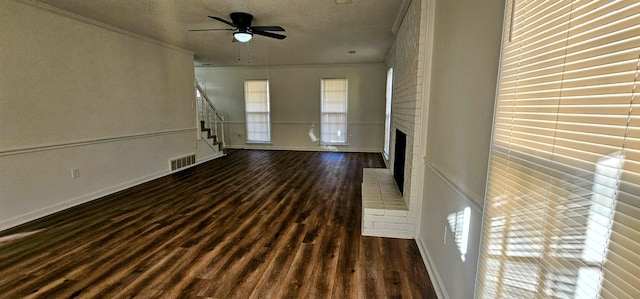 unfurnished living room featuring a brick fireplace, dark wood-type flooring, ornamental molding, and a textured ceiling