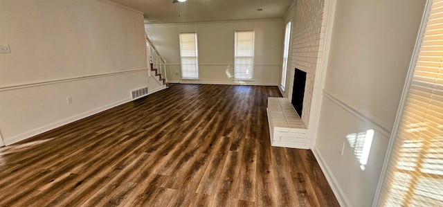 unfurnished living room featuring a brick fireplace, ornamental molding, dark hardwood / wood-style floors, and brick wall