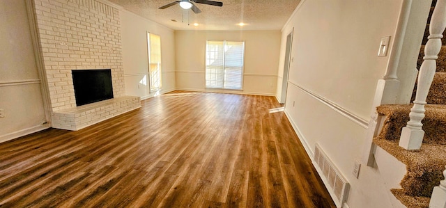 unfurnished living room featuring dark hardwood / wood-style flooring, ceiling fan, a fireplace, and a textured ceiling