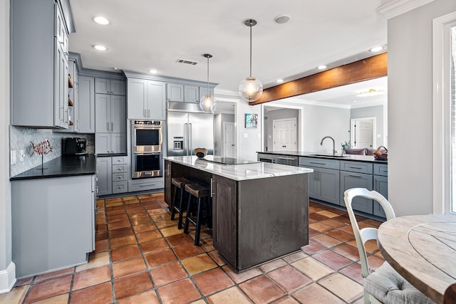 kitchen with a kitchen island, appliances with stainless steel finishes, pendant lighting, sink, and dark stone countertops